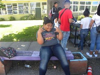 student sitting on bench smiling holding up the sign language sign for I love you